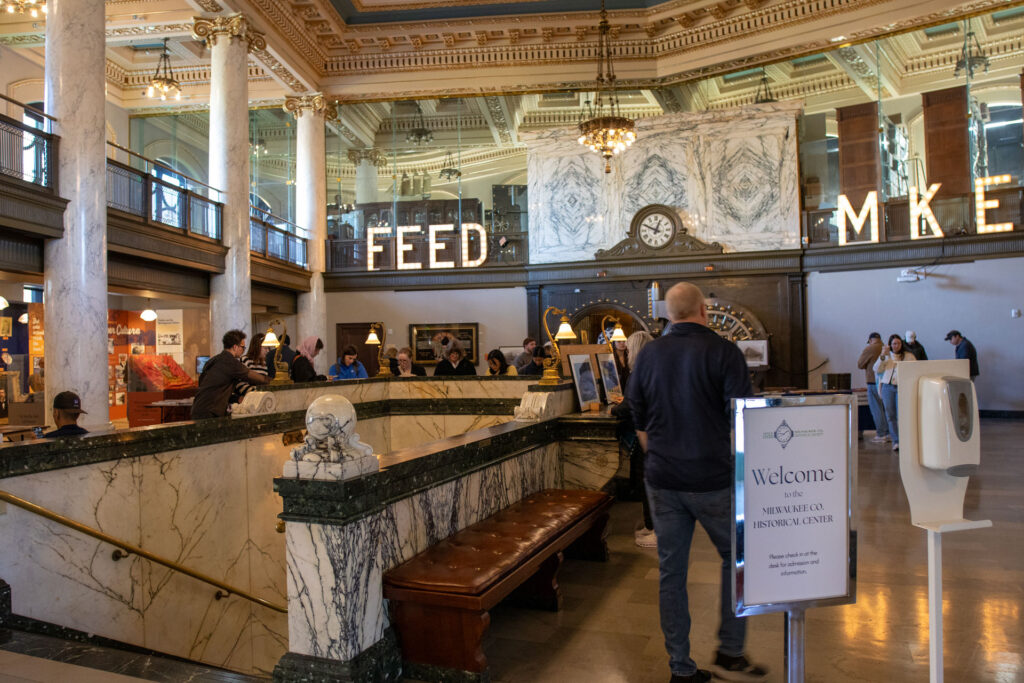 Visitors browsing book sale tables inside the marble lobby of the Milwaukee County Historical Society.