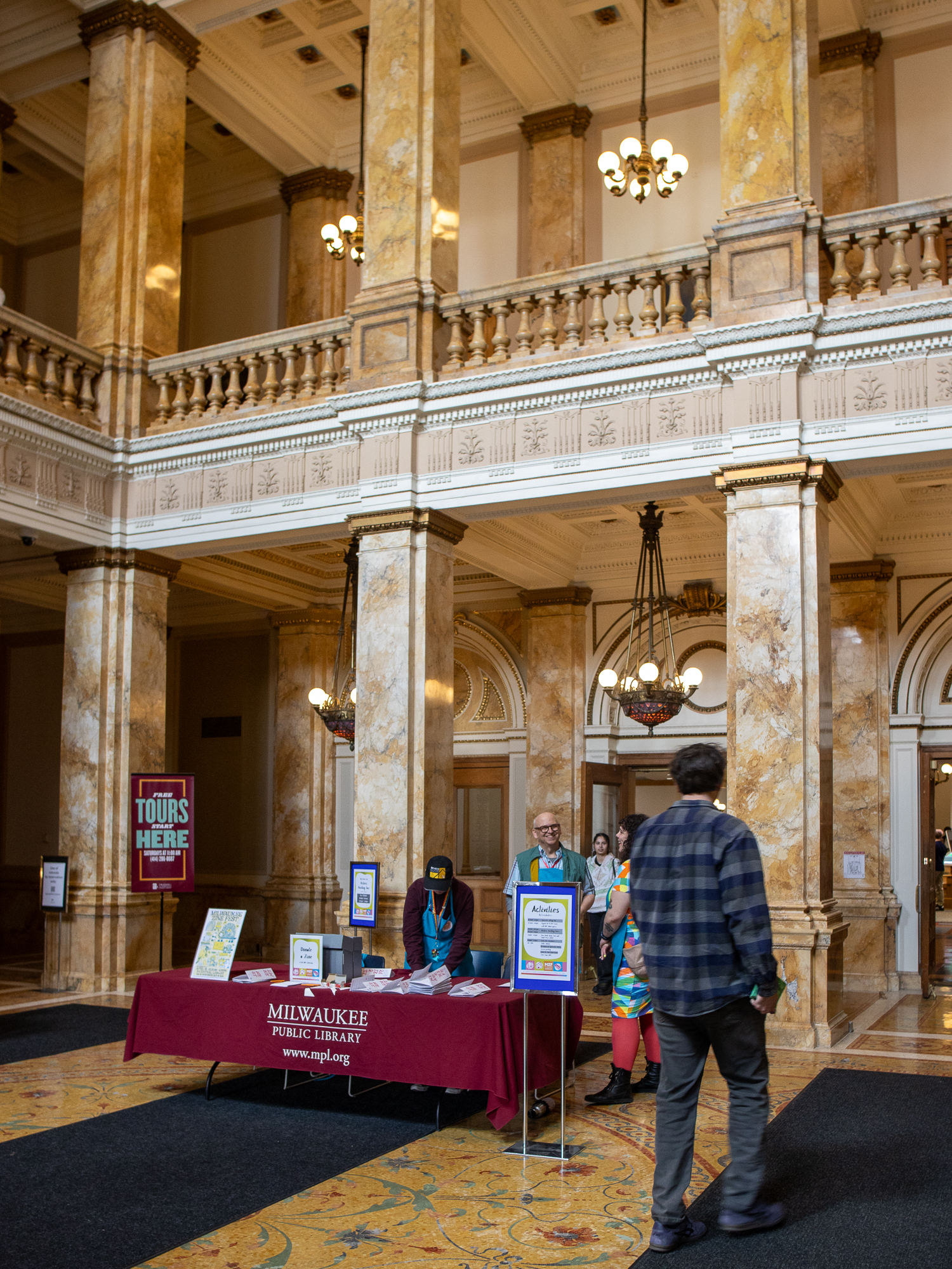 The grand rotunda interior of Milwaukee Central Library with a Milwaukee Public Library welcome table during Zine Fest