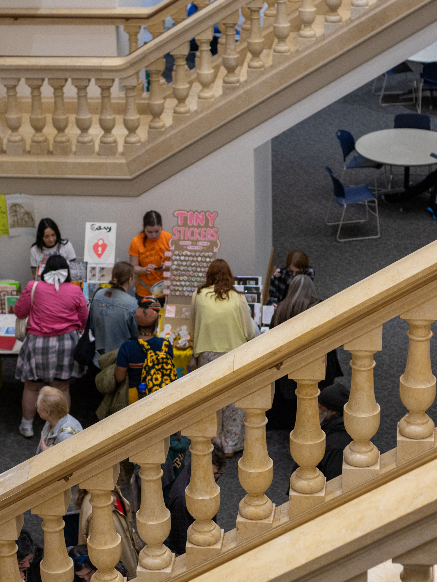 Looking down through the library staircase balustrade at vendor tables and attendees below