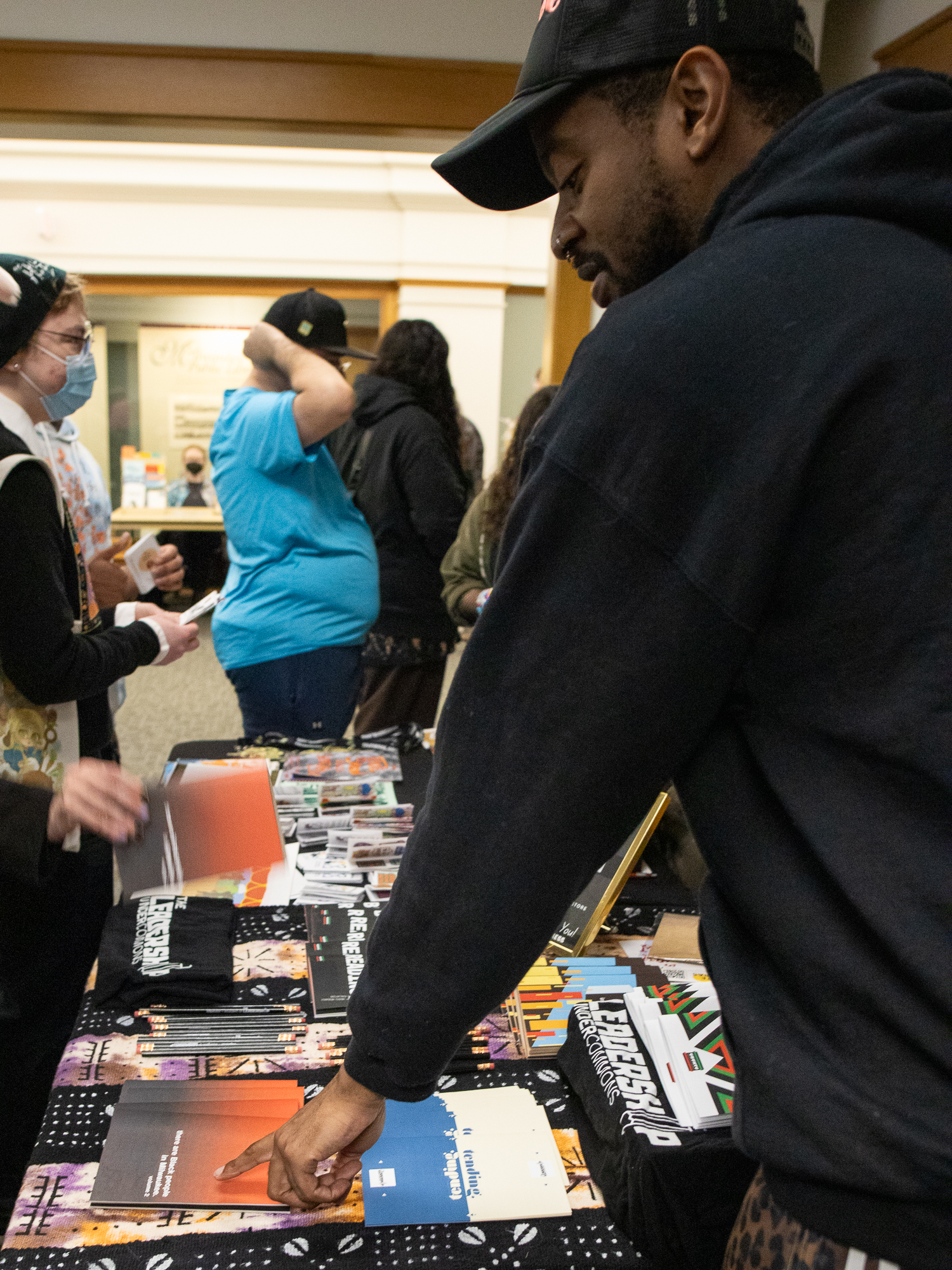 A vendor arranges zines on a table while an attendee browses at Milwaukee Zine Fest 2026