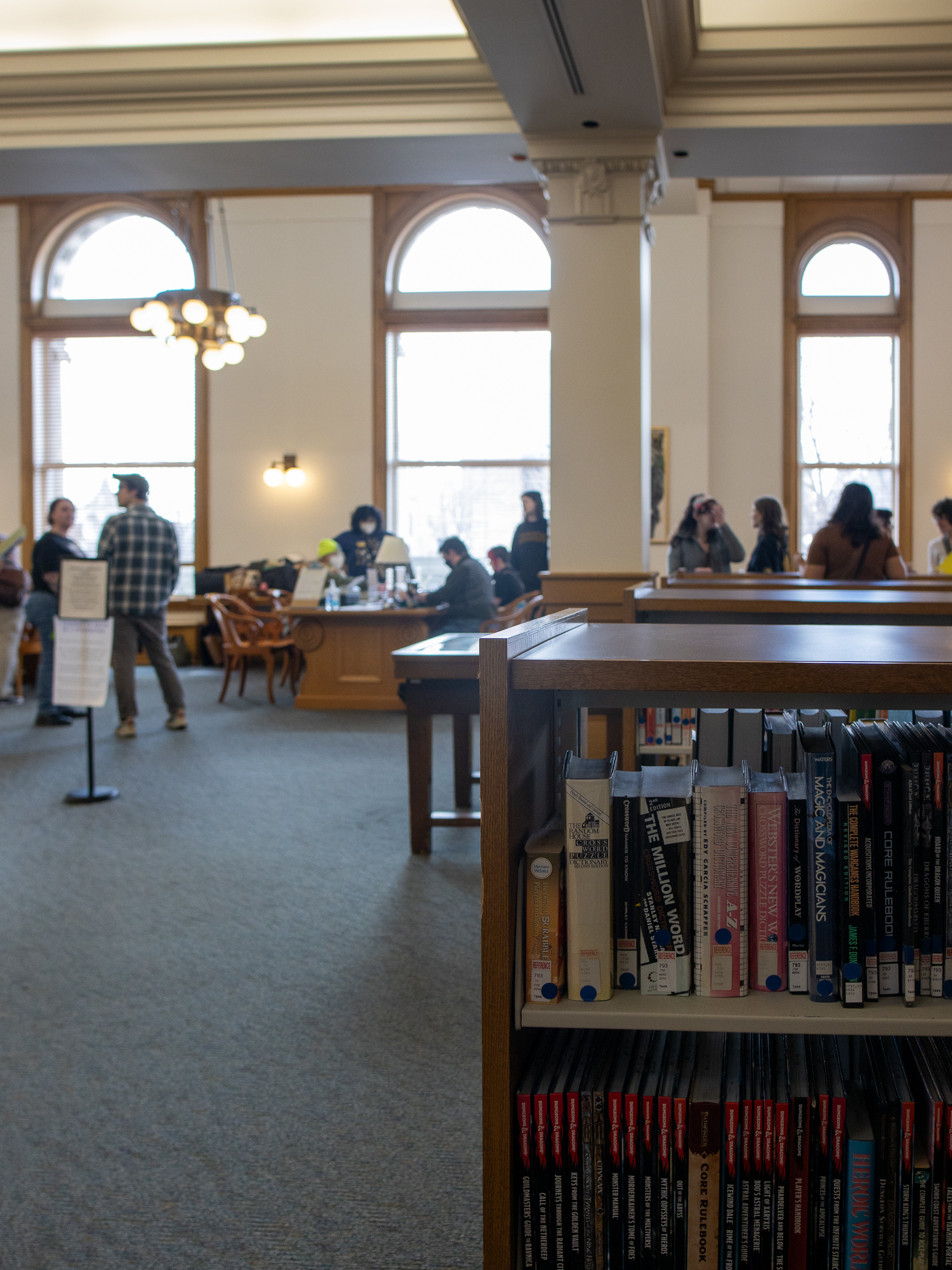 Library bookshelves in the foreground with people and typewriter tables blurred in a reading room behind